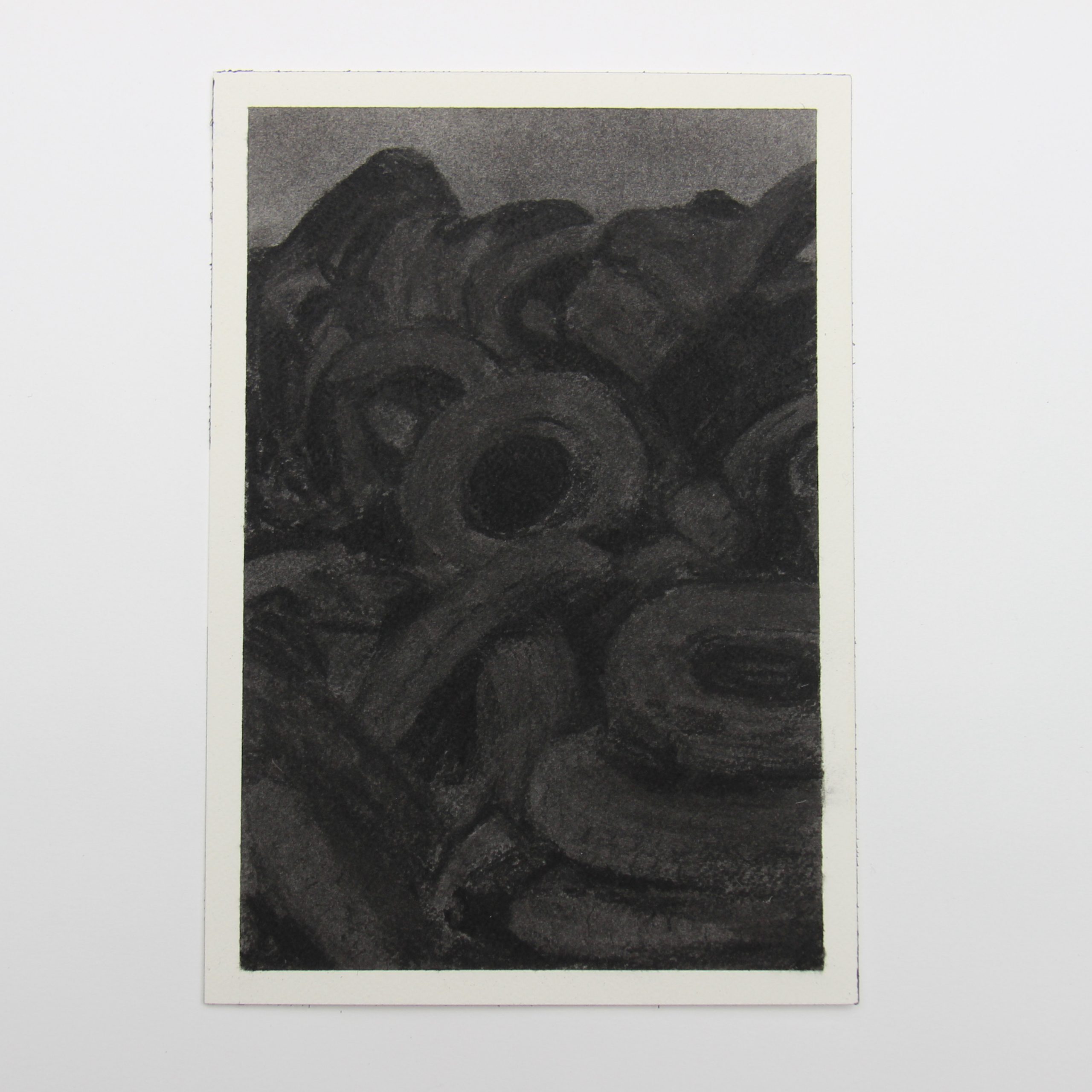 From a distance the drawing looks almost entirely black. When you move closer it reveals a dark landscape comprised of stacked rubber tires and a small area of dark sky all rendered in charcoal