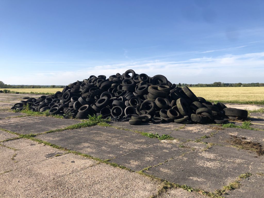 A pile of tyre's on concrete infront of a field and blue sky